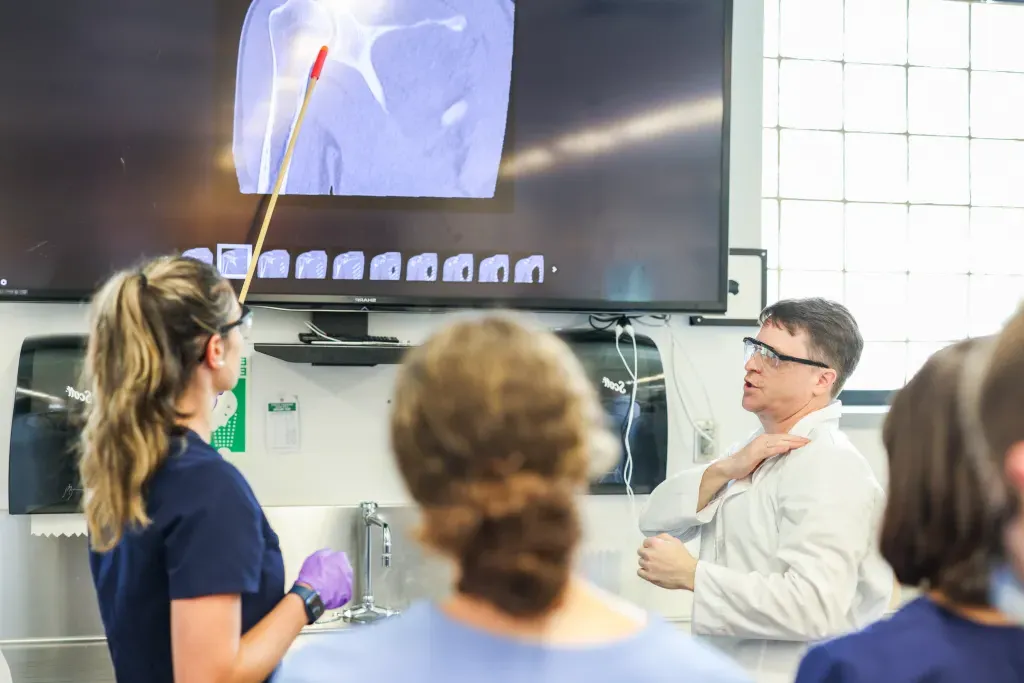 A student points to an anatomical image on a screen in front of their classmates