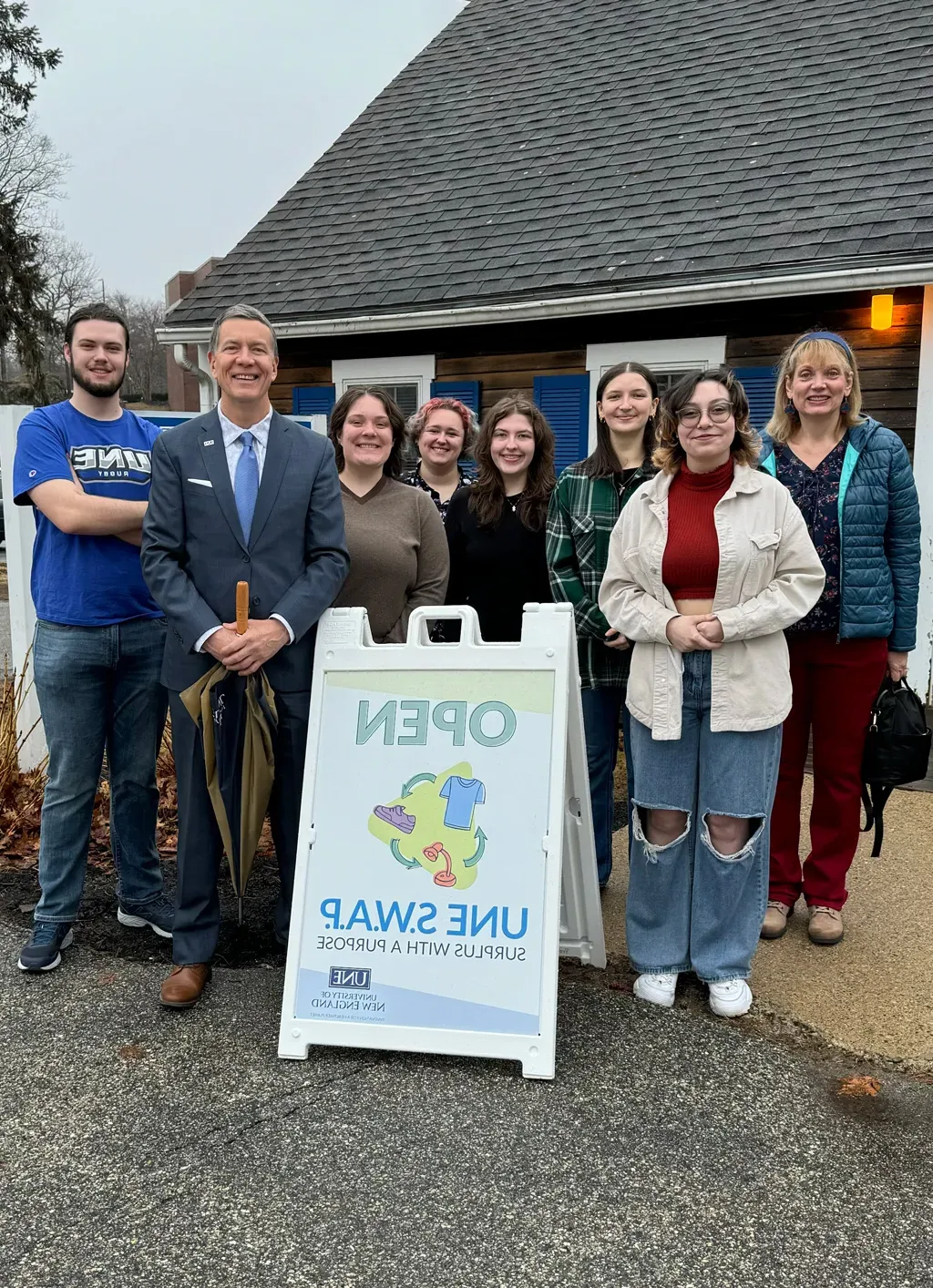 President Herbert stands with U N E students behind an "Open" sign for the Swap Shop