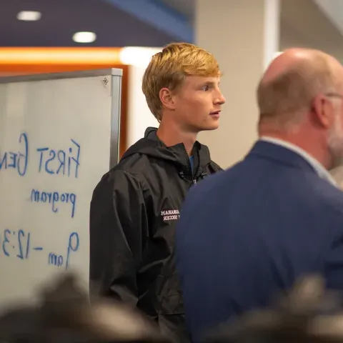 Student stands in front of sign for first-gen orientation.